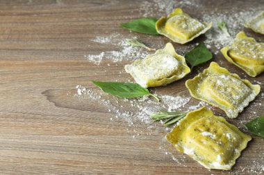 Ahşap zemin üzerinde un ve fesleğenli çiğ ravioli.