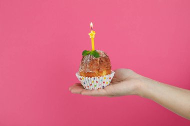 Kadın eli, pembe arka planda bir mum ile kek tutuyor..