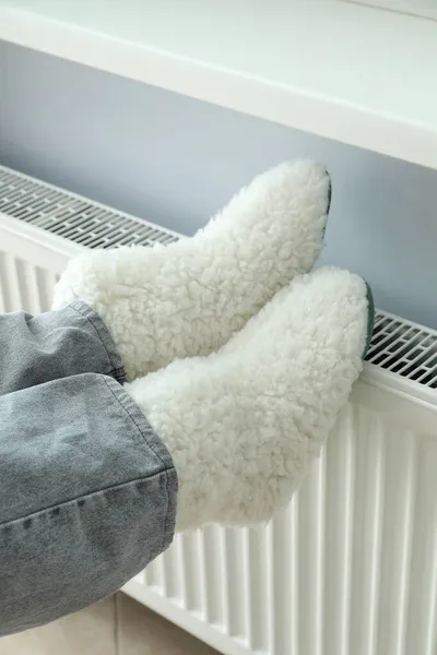 ラジエーターのニットブーツで足で暖房シーズンの概念 — ストック写真