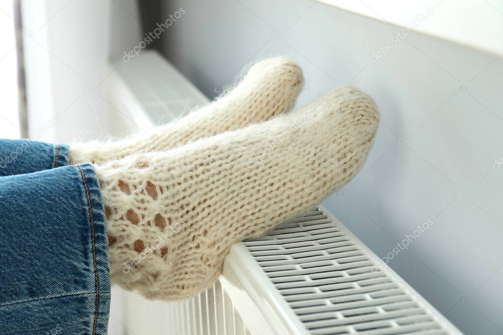 Concept of heating season with legs in knitted boots on radiator.