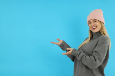 Süveter giyen çekici bir kız ve mavi arka planda örgü ören bir şapka..