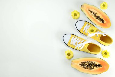 Çiçekli sarı spor ayakkabılar ve beyaz arka planda papaya.