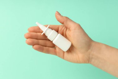 Kadın eli, arka planda boş burun spreyi şişesi tutuyor.