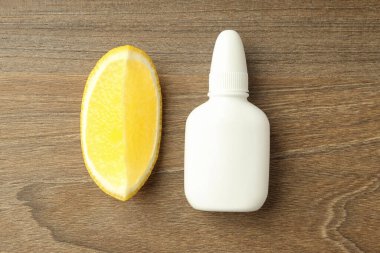 Boş burun spreyi şişesi ve ahşap arka planda limon dilimi.