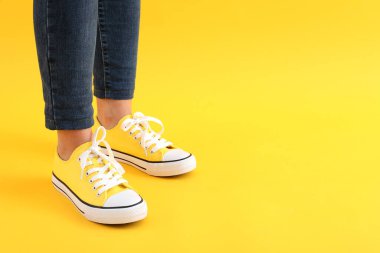 Kotlu kadın bacakları ve sarı arka planda spor ayakkabıları.