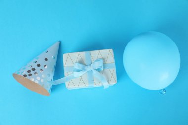 Hediye kutusu, parti şapkası ve balon mavi arka planda