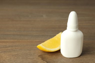 Boş burun spreyi şişesi ve ahşap arka planda limon dilimi.