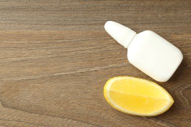 Boş burun spreyi şişesi ve ahşap arka planda limon dilimi.