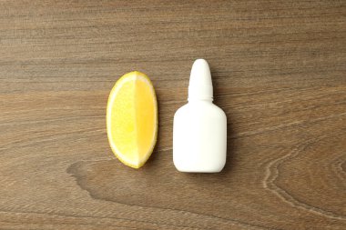 Boş burun spreyi şişesi ve ahşap arka planda limon dilimi.