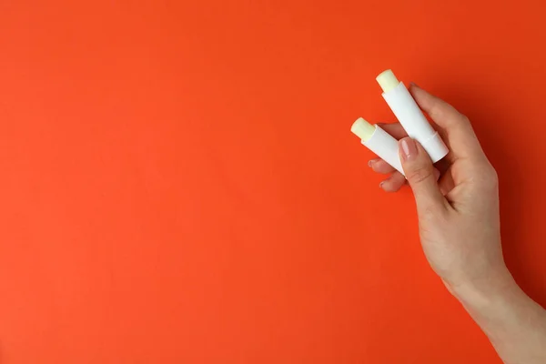 女性の手はオレンジの背景に衛生的な口紅を保持 — ストック写真