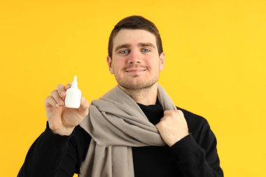 Sarı arka planda burun spreyi olan genç bir adam.