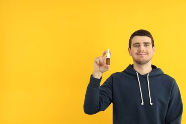 Sarı arka planda burun spreyi olan genç bir adam.