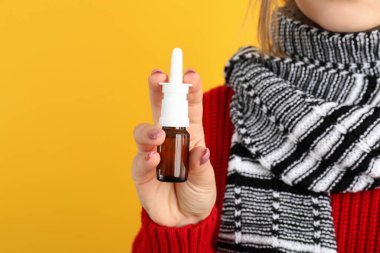 Sarı arka planda burun damlası olan genç bir kadın, burun akışı konsepti.