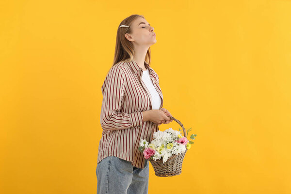 Attractive girl with basket of flowers on yellow background