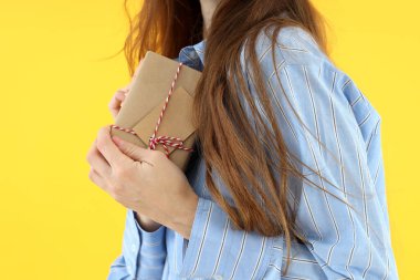 Gömlekli kadın sarı arka planda hediye kutusu tutuyor.