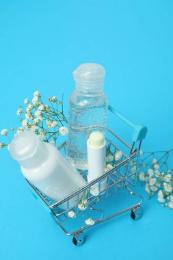 Mavi arka planda kozmetik ürünleri olan alışveriş arabası