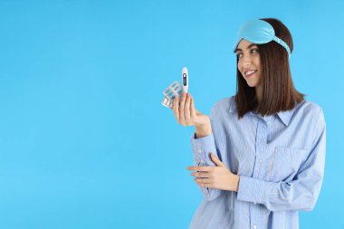 Mavi arka planda hapları ve termometresi olan çekici bir kadın.
