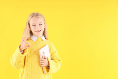Sarı arka planda defteri ve kalemi olan sevimli küçük bir kız.