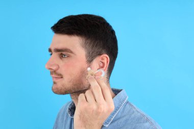 Genç adam mavi arka planda işitme cihazı tutuyor.