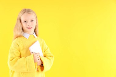 Sarı arka planda defteri ve kalemi olan sevimli küçük bir kız.