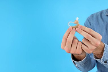 Elinde işitme cihazı tutan genç bir adam mavi bir arka planda.