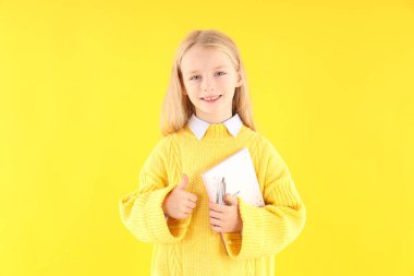 Sarı arka planda defteri ve kalemi olan sevimli küçük bir kız.