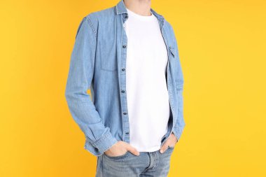 Boş tişörtlü ve sarı arka planda gömlekli bir adam.