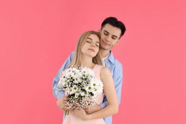 Pembe arka planda buketi olan sevimli bir çift.