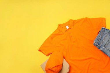 Sarı arka planda pizza kutusu olan boş bir teslimatçı üniforması.