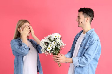 Bir erkek pembe arka plandaki bir kıza buket verir.