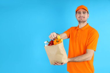 Teslimatçı mavi arka planda yiyecek dolu bir çanta tutuyor.