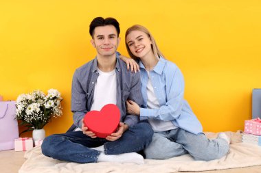 Sarı arka planda oturan sevimli ve mutlu bir çift.