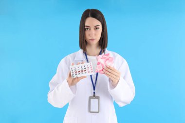Female doctor with period calendar and pads on blue background