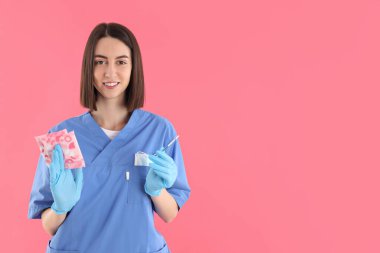 Female nurse with pads and pregnancy test on pink background