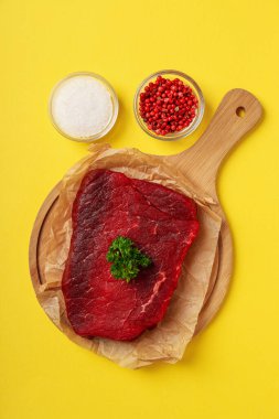 Concept of cooking with raw steak on yellow background