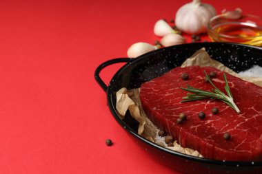 Kırmızı arka planda çiğ biftek pişirme kavramı