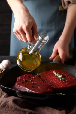 Woman chef pour oil on raw beef steaks
