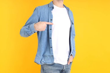 Boş tişörtlü ve sarı arka planda gömlekli bir adam.