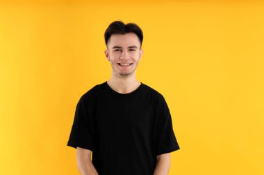 Sarı arka planda tişörtlü çekici bir genç.