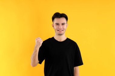 Sarı arka planda tişörtlü çekici bir genç.