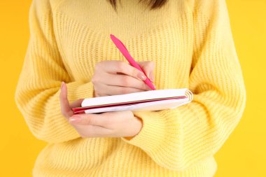 Sarı arka planda defteri olan genç bir kız.