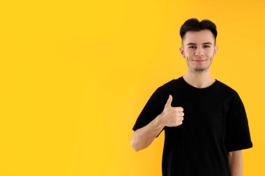 Sarı arka planda tişörtlü çekici bir genç.