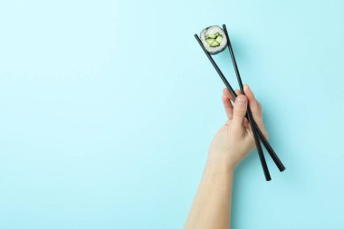 Kadın eli mavi arka planda yemek çubuklarıyla suşi tutuyor.