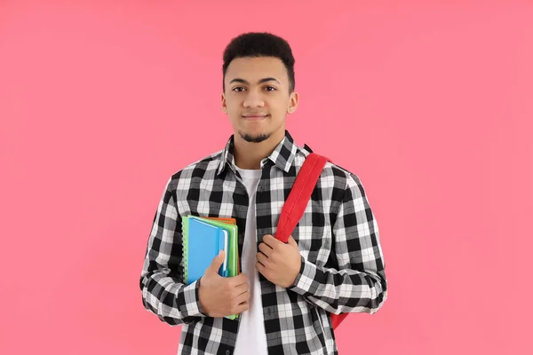 Male student with notebooks and backpack on pink background