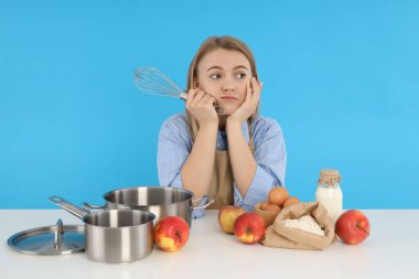 Genç bayan şef oturuyor ve mavi arka planda sıkılıyor.