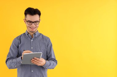 Sarı arka planda not defteri ve kalemi olan çekici bir adam.