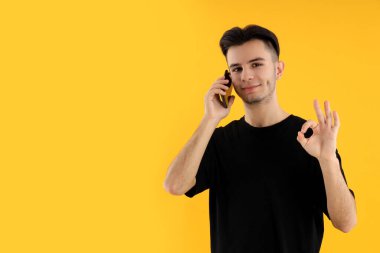 Sarı arka planda genç adam telefonda konuşuyor.