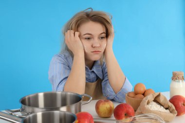 Genç bayan şef oturuyor ve mavi arka planda sıkılıyor.