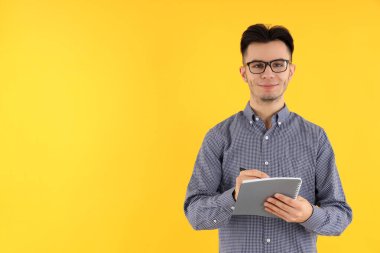 Sarı arka planda not defteri ve kalemi olan çekici bir adam.