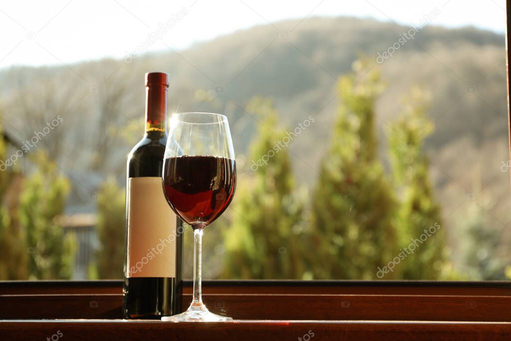 Glass and bottle of wine stands on wooden windowsill